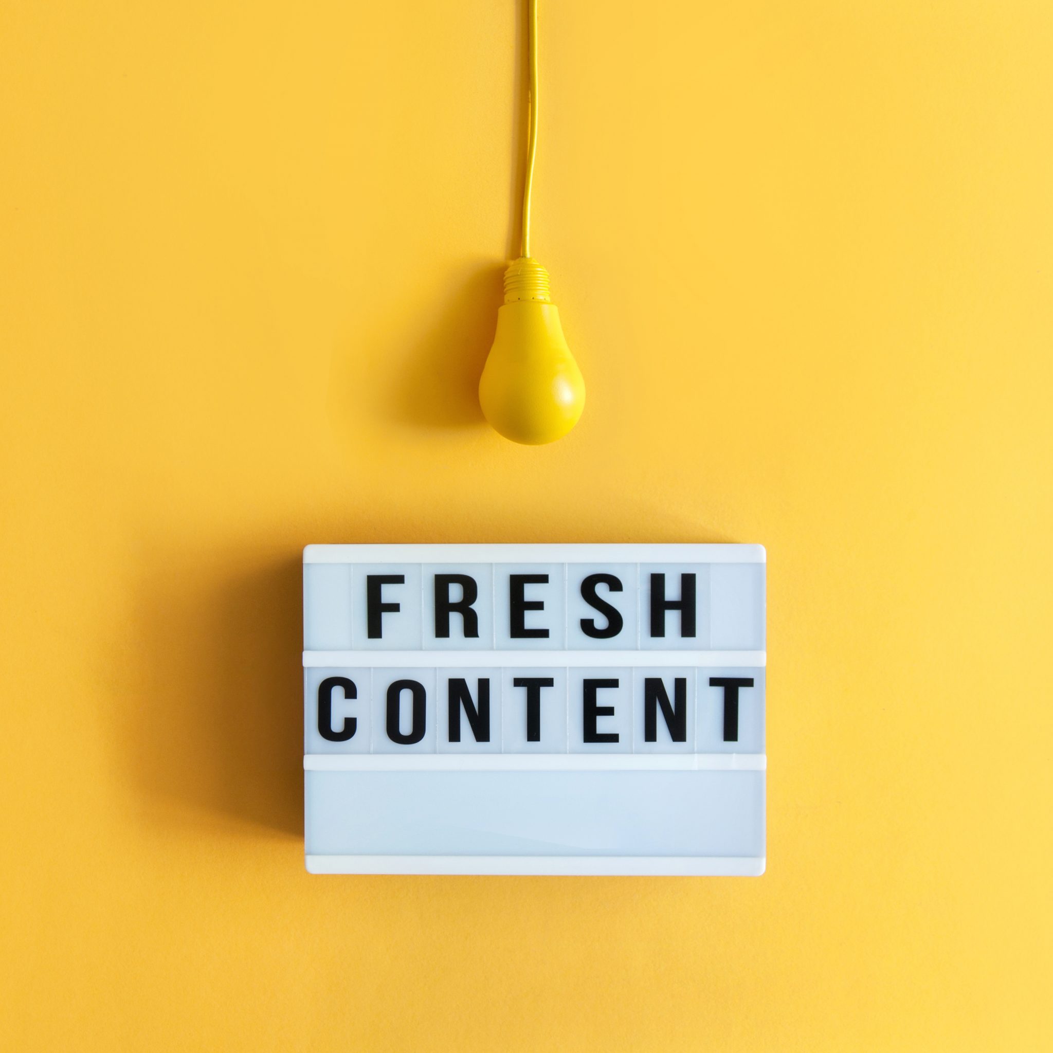 A yellow lightbulb hanging over a sign that says "FRESH CONTENT" on a yellow background.